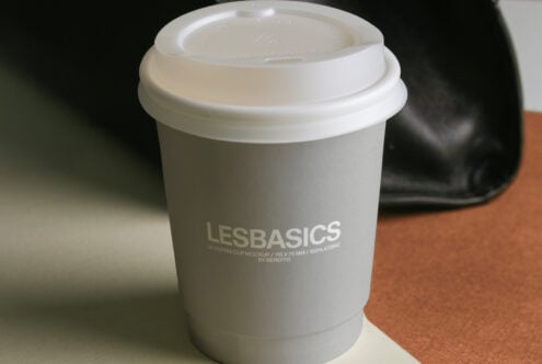 White coffee cup with lid close-up shot on tan surface with leather bag behind