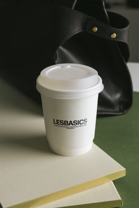 White coffee cup with lid staged on green notebook with black leather bag backdrop