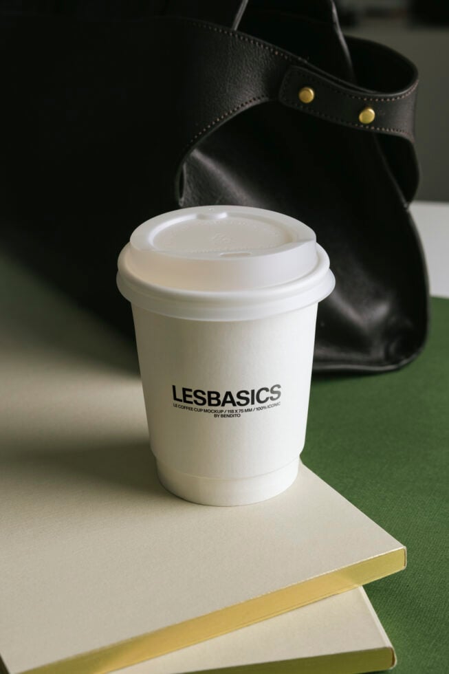 White coffee cup with lid staged on green notebook with black leather bag backdrop