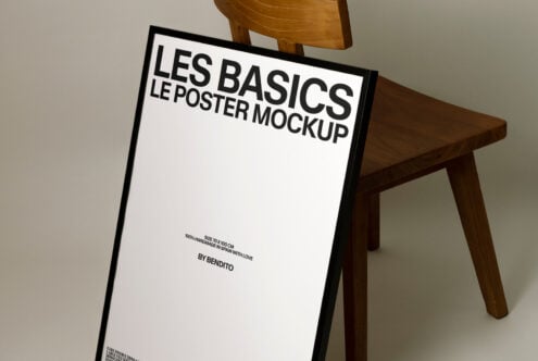 Poster mockup with black frame leaning against wooden chair in studio