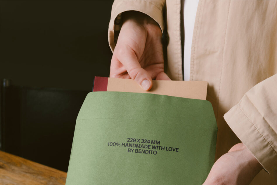 Close-up of hand holding green envelope mockup over wooden surface