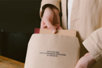 Close-up of hand holding cream envelope mockup over wooden surface
