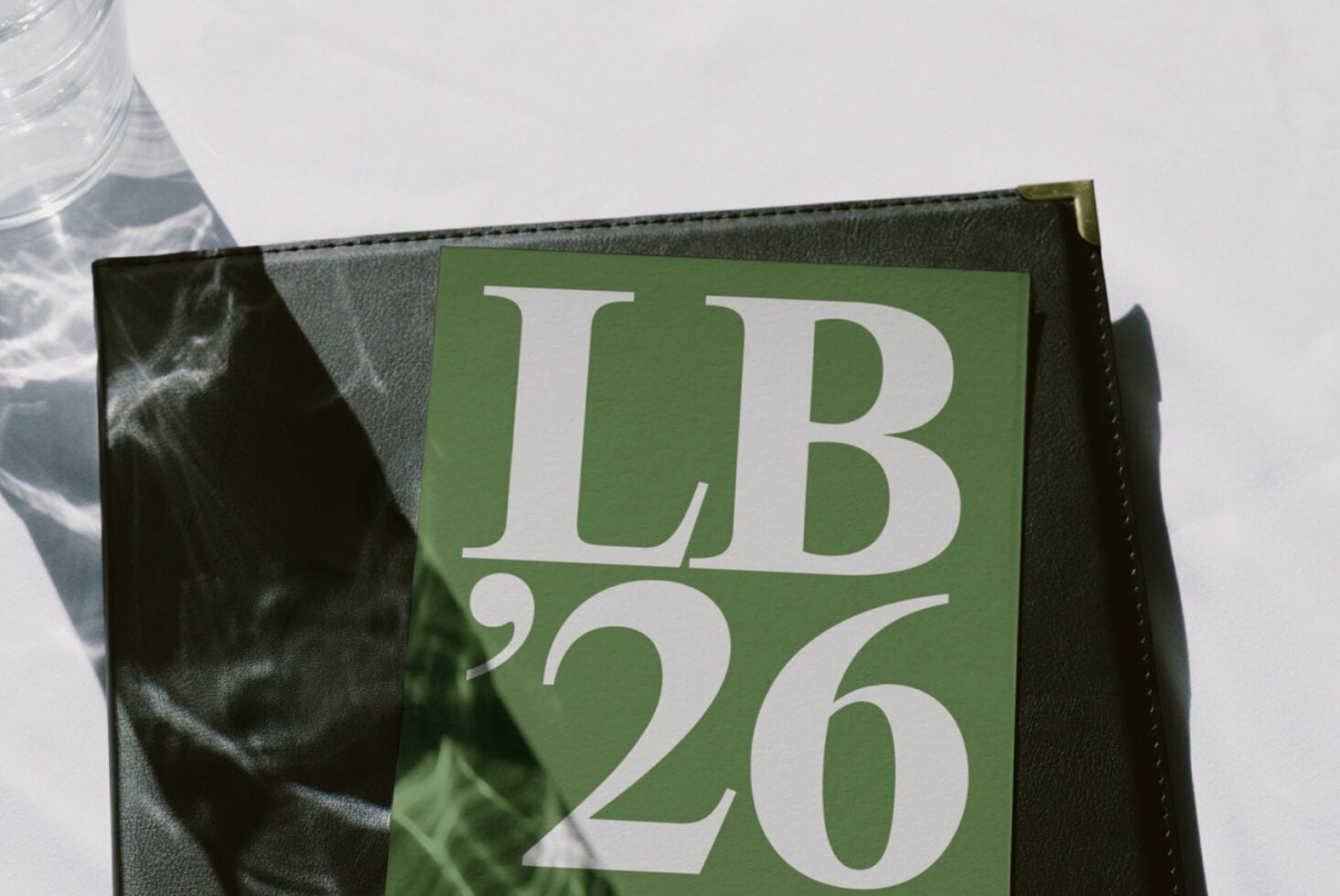 Sage green menu card nested in dark leather holder on white background