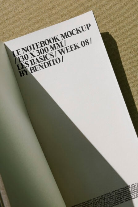 White notebook mockup angled on beige textile surface with dramatic shadow