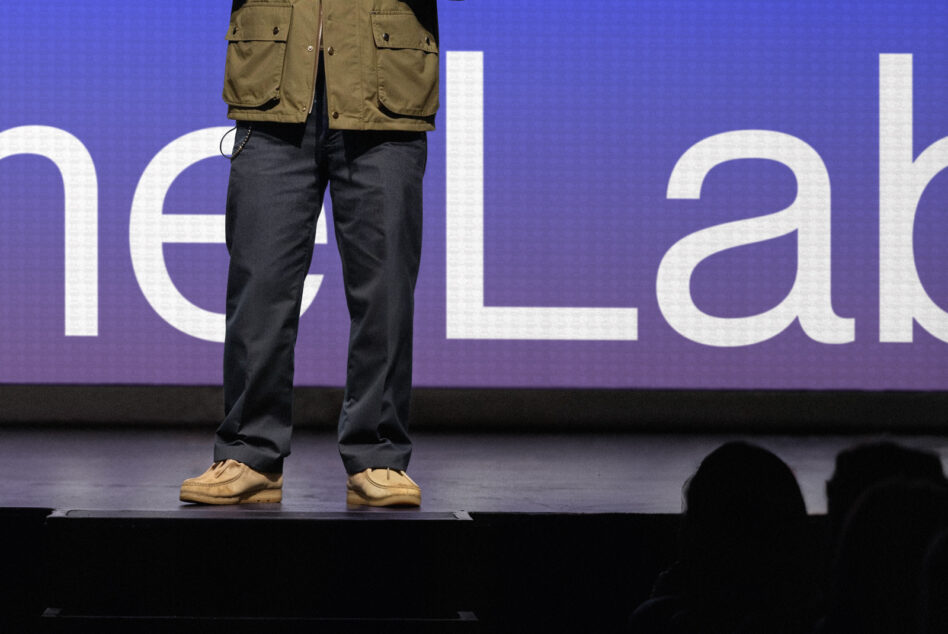 Close-up of legs on stage with khaki jacket, dark jeans, tan shoes