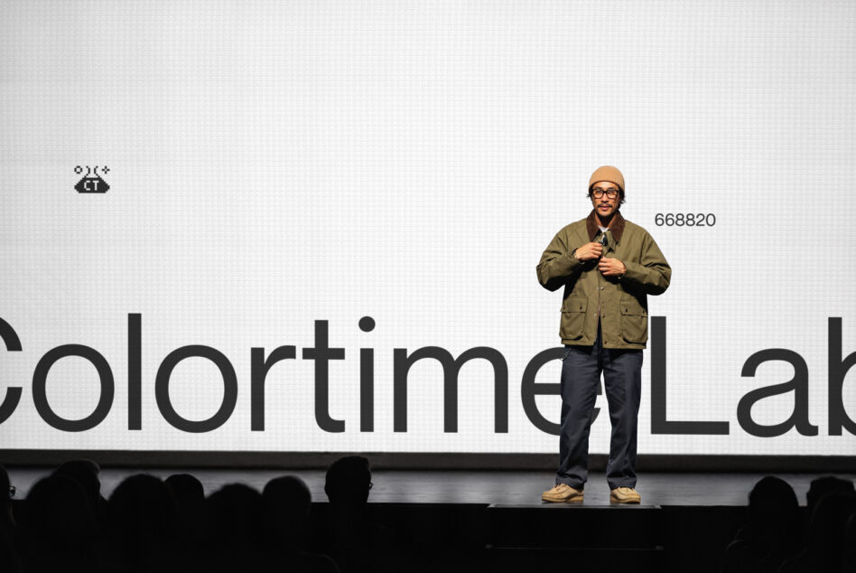 Person in tan jacket on stage with partial text display behind them
