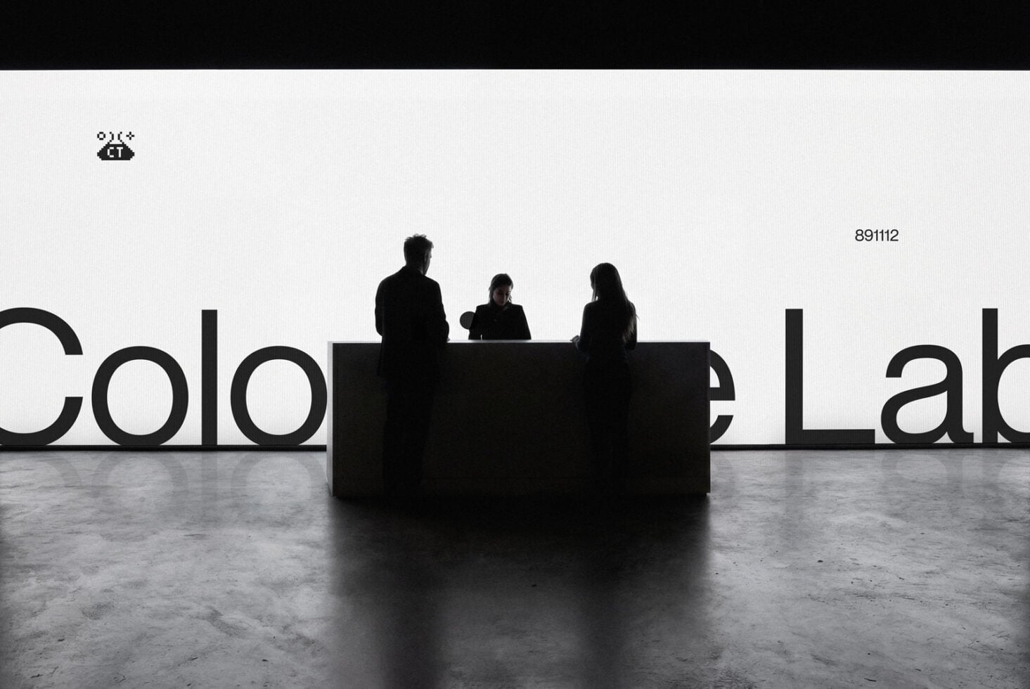 Three silhouetted figures sitting behind black desk with large partial text visible behind them