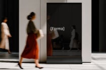 Black digital display screen with (forma) text in minimalist hallway with walking figures
