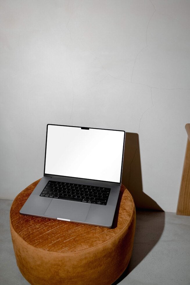 Laptop with blank white screen sitting on wooden round side table