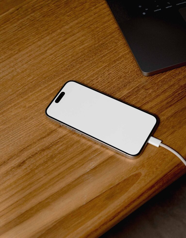 iPhone with blank screen on wooden desk next to charging cable