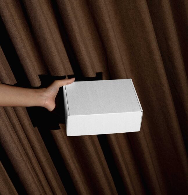 Hands holding closed white box against brown fabric backdrop