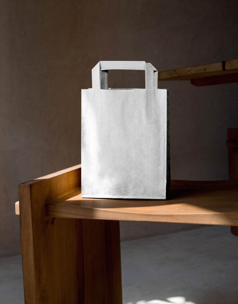 Blank white kraft paper bag with handles sitting on wooden table