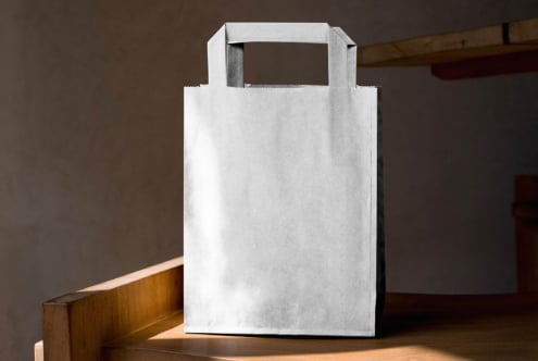 Blank white paper bag with scalloped edge trim on wooden table