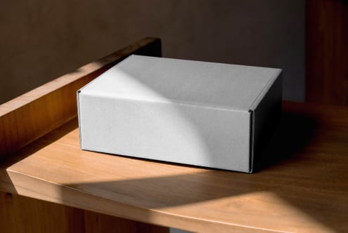 White rectangular box on wood table lit by window light, minimal styling