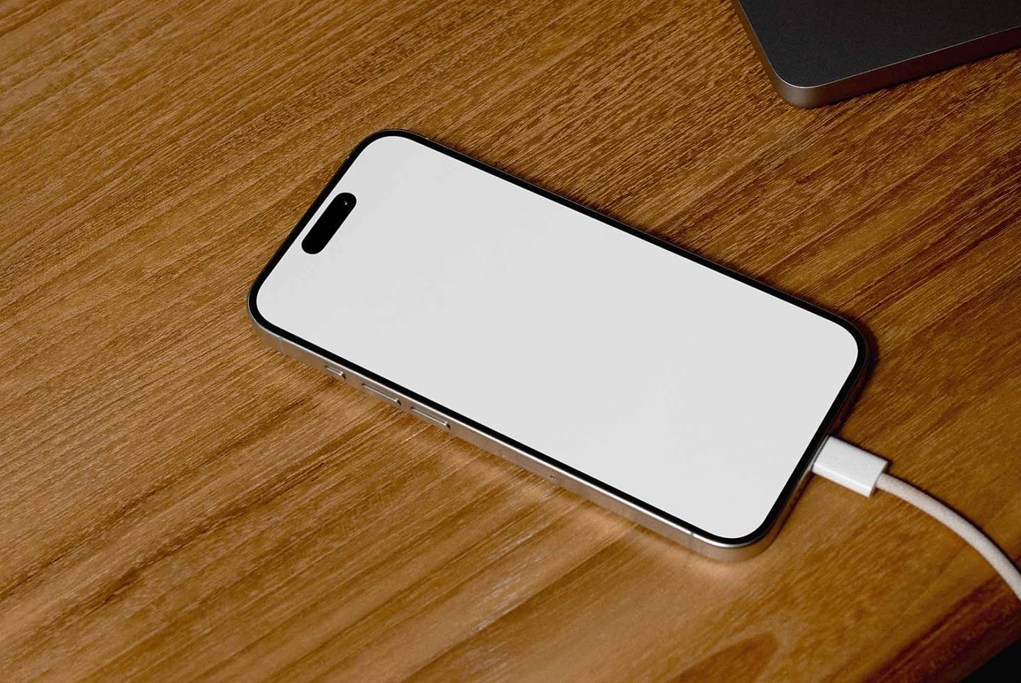 iPhone lying on wood surface showing empty white display with USB-C port