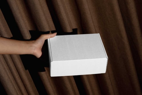 Hands holding open white box showing inside against brown fabric