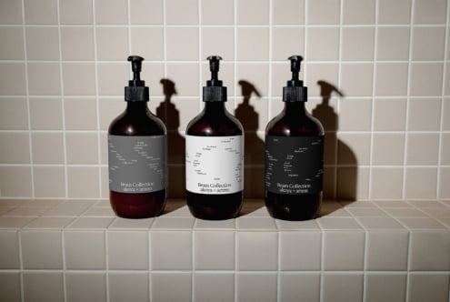 Three dark glass dispenser bottles displaying Beam Collection labels on neutral tile surface