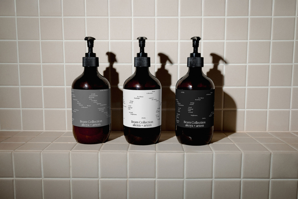 Three dark glass dispenser bottles displaying Beam Collection labels on neutral tile surface
