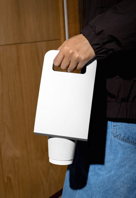 Hand gripping white handle bag mockup with blank label next to cylindrical product