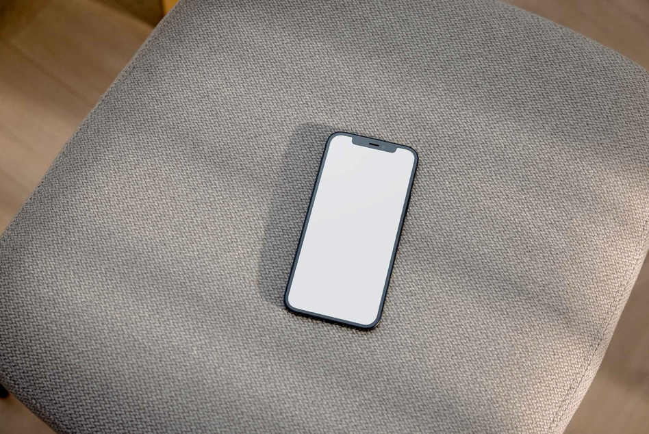 Smartphone with blank screen resting on gray fabric surface, flat lay
