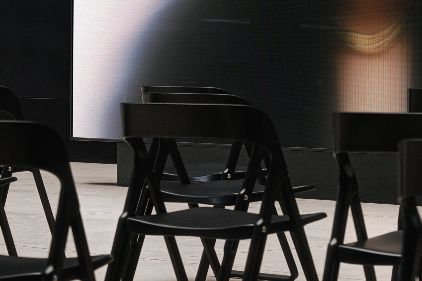 Black chairs facing blank dark projection screen in minimalist interior