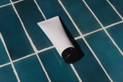 White cosmetic tube with black cap on teal grid tile background