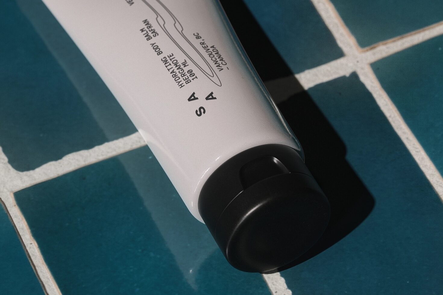 White cosmetic tube with black cap on teal tile surface