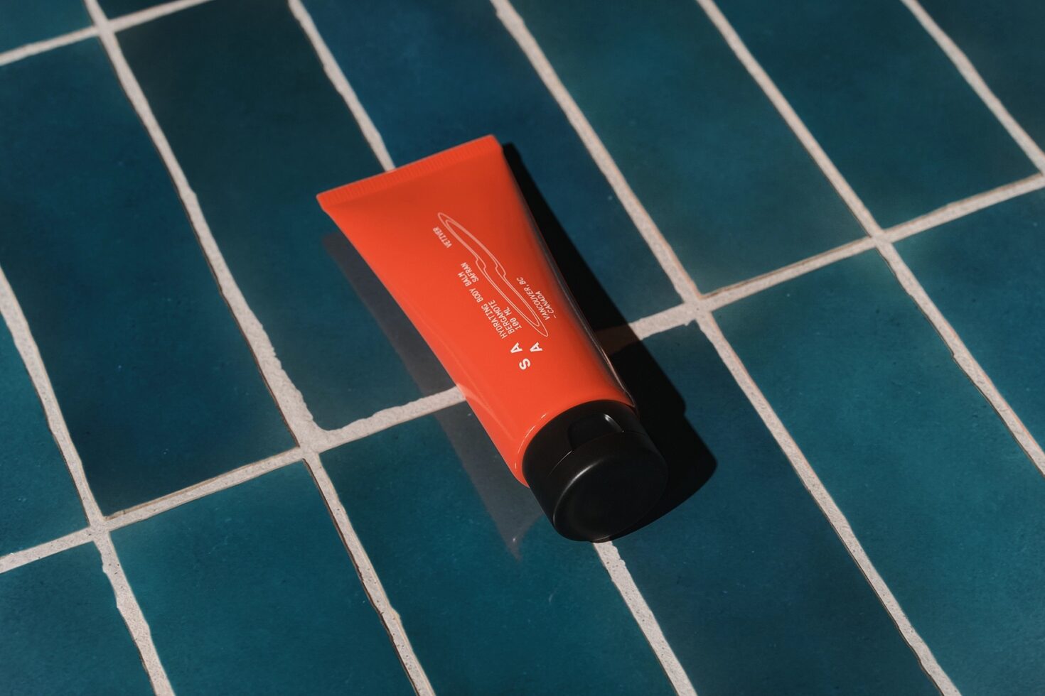 Bright orange beauty tube mockup sitting on teal grid tile layout