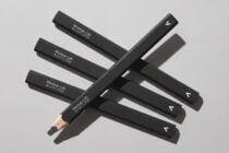 Dark pencils stacked in geometric layout on neutral gray surface with sharp shadows