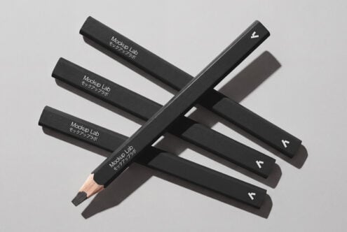 Dark pencils stacked in geometric layout on neutral gray surface with sharp shadows