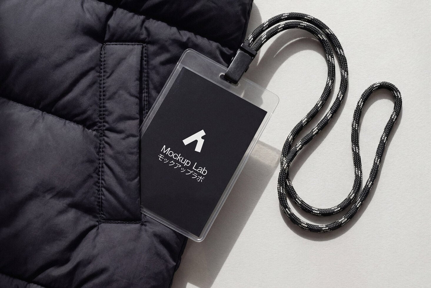 Dark ID card with white logo hanging from metallic braided lanyard on white fabric