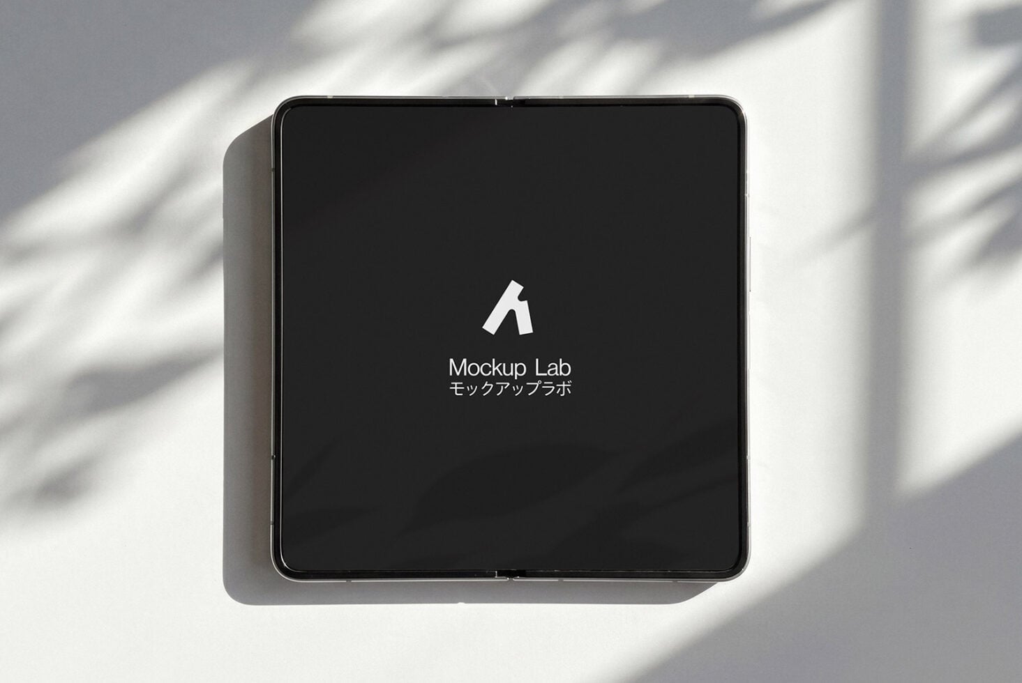 Square tablet device displaying dark screen with white logo in bright sunlight