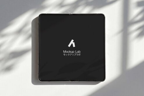 Square tablet device displaying dark screen with white logo in bright sunlight