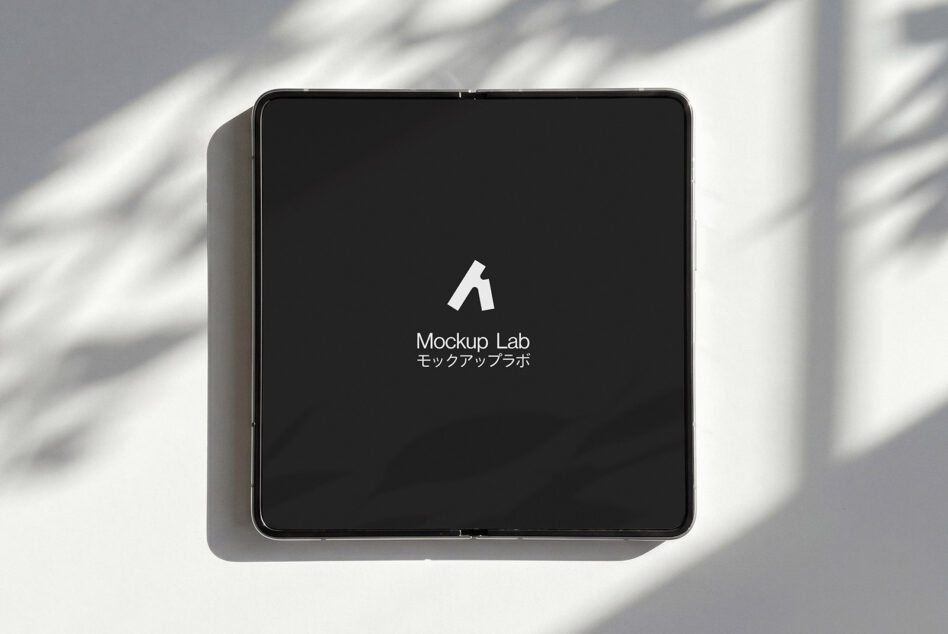 Square tablet device displaying dark screen with white logo in bright sunlight