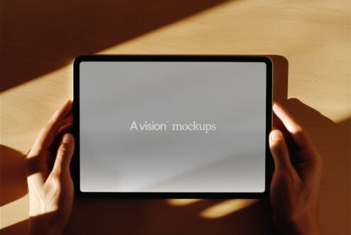 Hands holding horizontal tablet with soft gray display on wooden surface