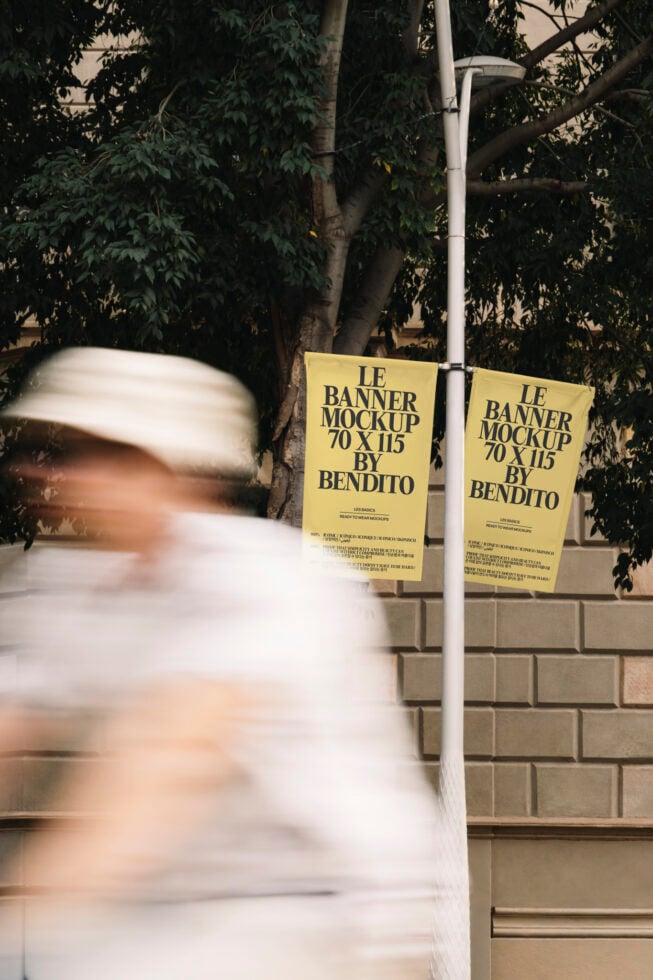 Two yellow hanging banner mockups on street pole with blurred person walking