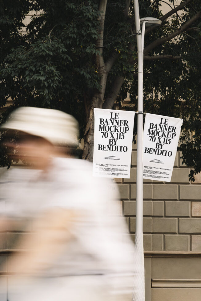 Two white hanging banner mockups on street pole with blurred person walking