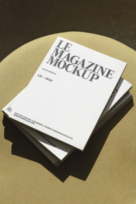 Stacked cream magazine mockups tilted on pale yellow round surface with dramatic lighting
