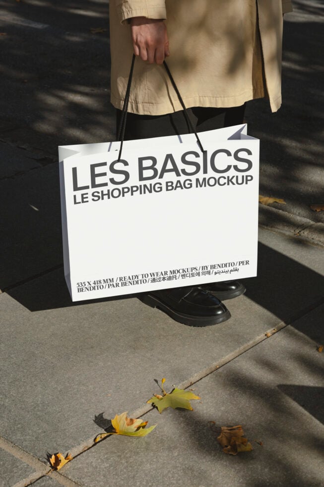 White shopping bag mockup held by person in neutral outfit on street