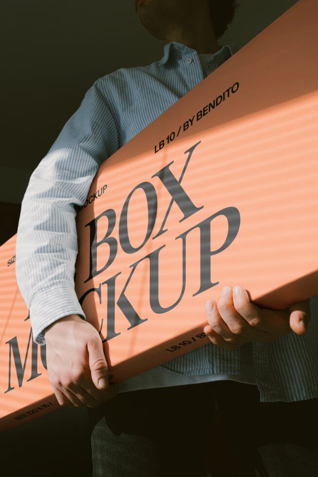 Person holding peach colored box mockup at angle with dramatic shadow lighting