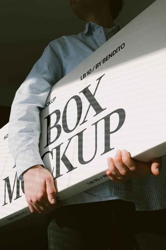 Person holding white box mockup at angle with dramatic shadow lighting
