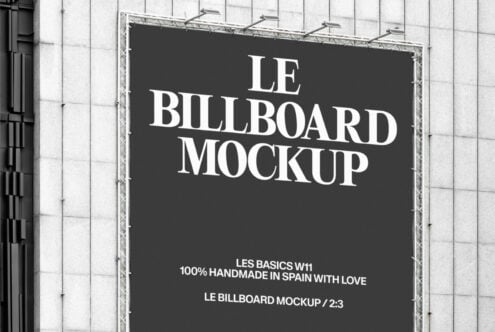 Wide shot of black billboard displaying Le Billboard Mockup text on white grid building facade