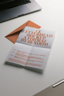 Folded letterhead with orange envelope on desk next to laptop