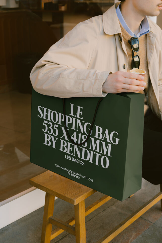Green paper shopping bag with white text held by person in beige jacket
