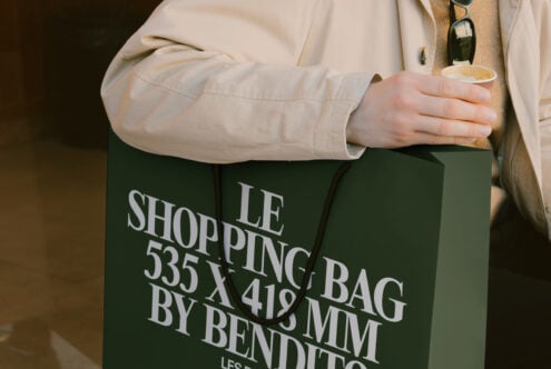 Close up of green shopping bag with white typography held against cream coat