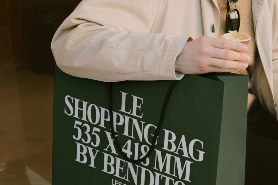 Close up of green shopping bag with white typography held against cream coat