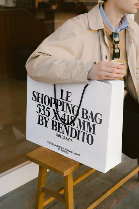 White paper shopping bag with black text held by person in beige jacket