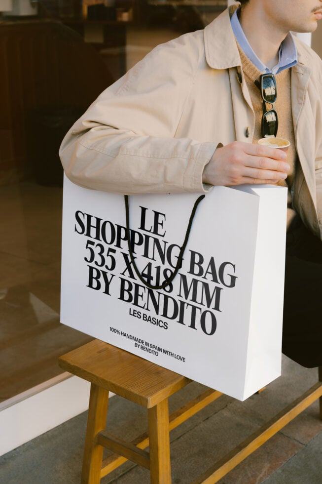 White paper shopping bag with black text held by person in beige jacket