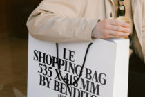 Close up of white shopping bag with black typography held against cream coat