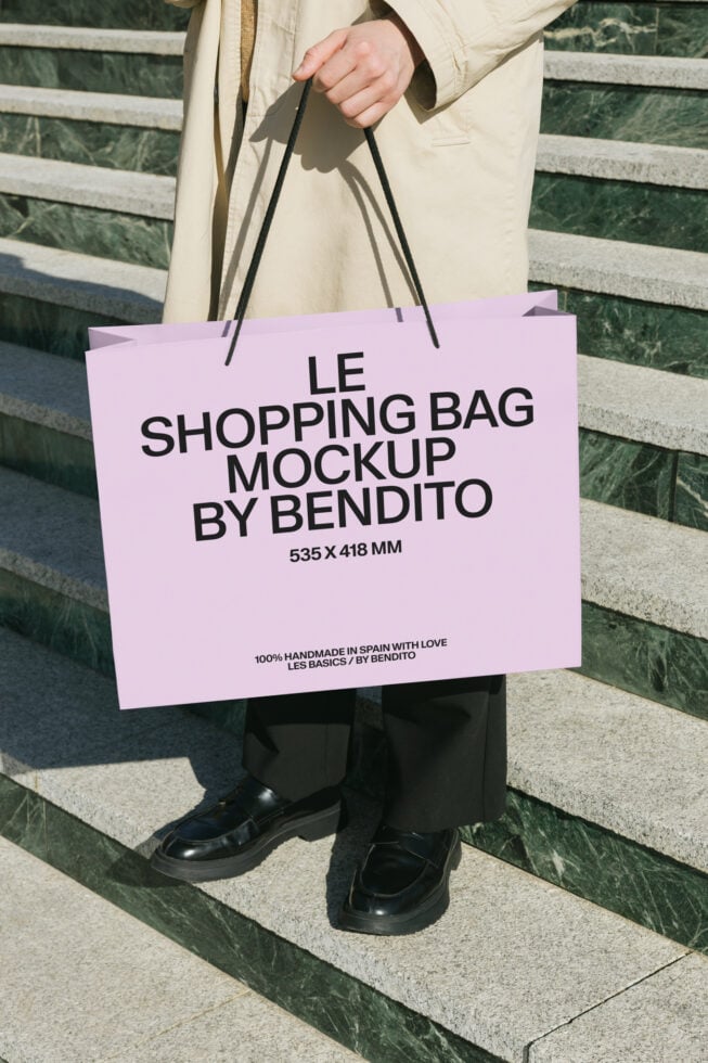 Person holding pink shopping bag mockup in beige coat outdoors